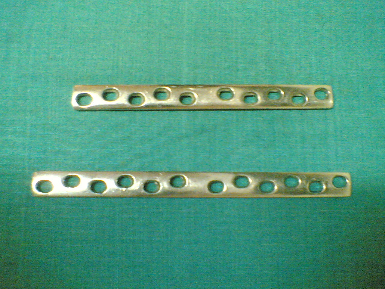 Figure 5. Broad dynamic compression plates, showing the characteristic angled oval holes through which the sliding screw head produces axial compression. Source: Netha Hussain, via Wikimedia Commons, CC BY-SA 3.0.